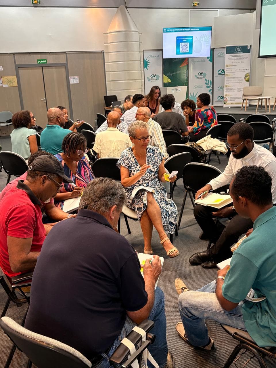 Participants en atelier collaboratif sur les bioressources, en discussion par petits groupes, avec écran de synthèse et bannières